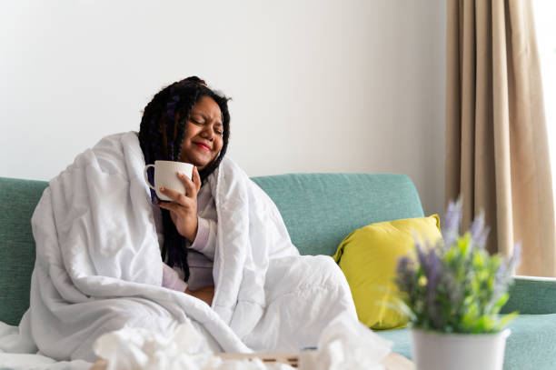 istock Young woman relaxing on sofa with hot drink, feeling sick 2198568616