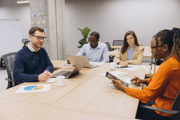 istock Diverse group of professionals engaged in a collaborative business meeting, using laptops and tablets, discussing charts and data in a modern office 2198569957