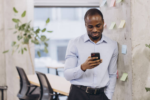 istock Professional african american leaning against wall, surrounded by sticky notes, working on smartphone in modern workspace, embodying digital efficiency 2198570830