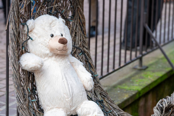 Cute white teddy bear leaning against an outdoor Christmas display