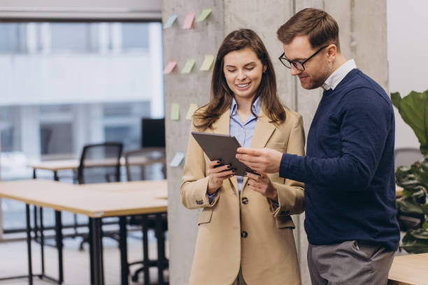istock Two professionals man and woman discussing work on a tablet in a contemporary office, surrounded by sticky notes and modern furniture, fostering teamwork 2198570965