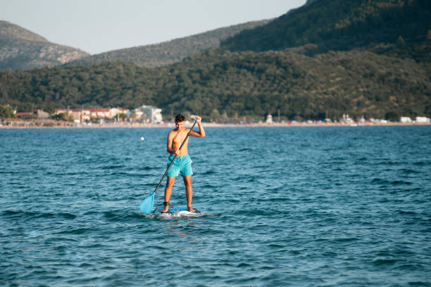 Young man driving stand up paddle board at the sea