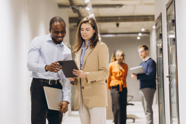 istock Interracial business people using digital tablet and laptop, walking in office corridor, discussing work 2198573251