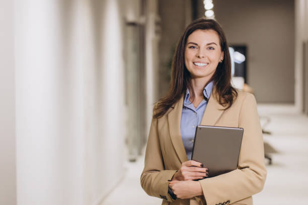 istock Businesswoman smiling while holding a tablet, exuding confidence in a modern office corridor, embodying professionalism and success 2198573313