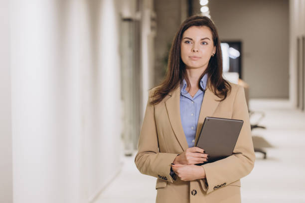 istock Businesswoman holding a tablet while walking through an office corridor, looking away with a confident and elegant demeanor 2198573314