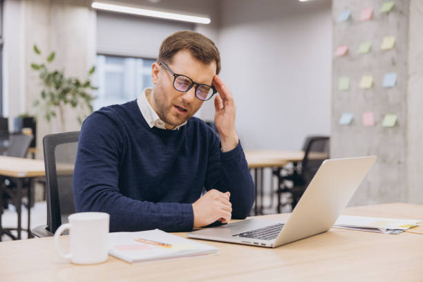istock Office male worker suffering from headache while using laptop, touching his head with hand, sitting at desk in modern office 2198573407