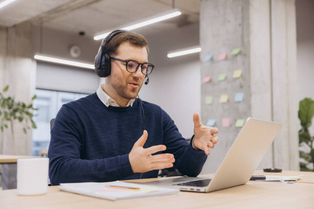 istock Professional male worker communicating during video call, wearing headset, glasses in contemporary workspace 2198573574