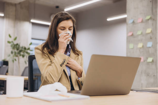 istock Professional woman experiencing flu symptoms, wiping nose near computer during workday 2198575838