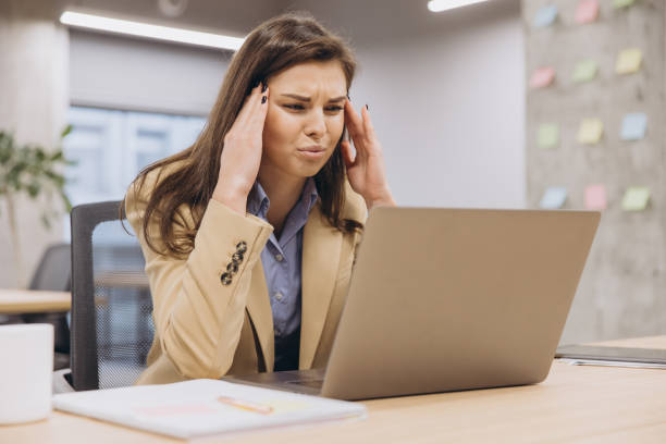 istock Young businesswoman suffering from headache while working on laptop in office, concept of stress and overwork in corporate environment 2198575843