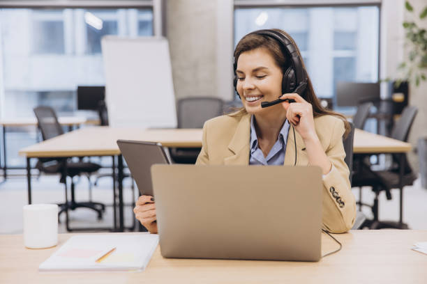 istock Happy female manager wearing headset and using laptop and tablet while working in modern office 2198576031