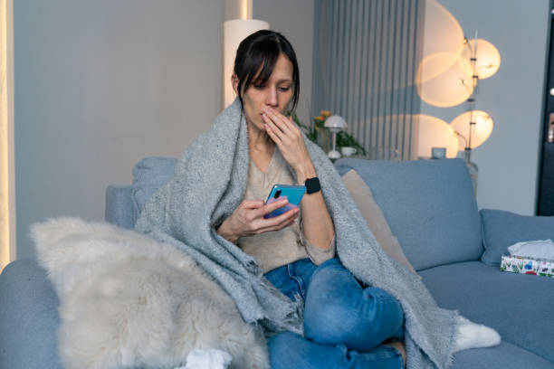istock White woman sitting on couch with headache holding smartphone 2198580030