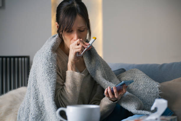 istock Feverish woman sitting on sofa checking symptoms on mobile phone 2198580215