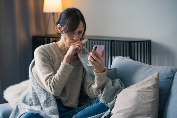 istock Ill woman sit on a sofa hold holding smartphone and thermometer 2198580339