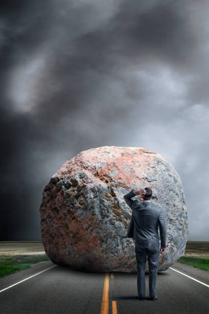 istock Businessman Stands Looking At Large Boulder Blocking His Path In Middle Of Road 2198581319