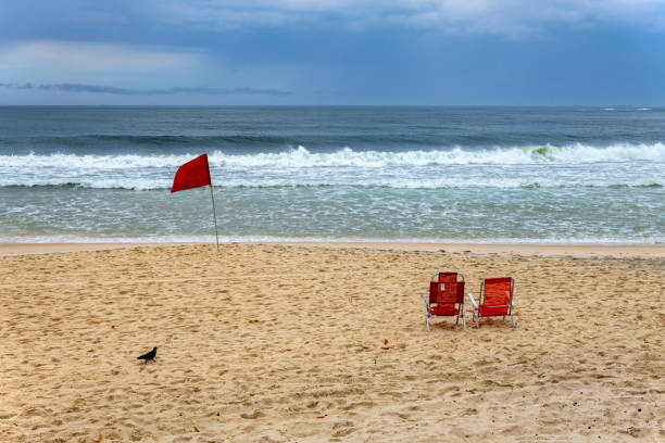 Rio de Janeiro, Brazil, November 8, 2024: View of the deserted Copacabana beach in windy cloudy weather. The red flag means no swimming allowed.