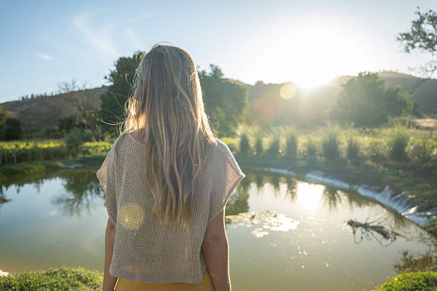 istock Woman Enjoying Serene Sunset by Tranquil Pond 2198587426