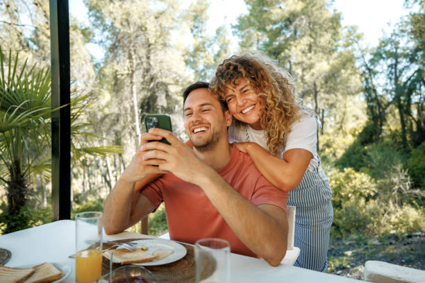 Cheerful young couple using smart phone while having breakfast outdoors