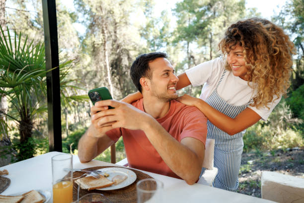 istock Cheerful young couple using smart phone while having breakfast outdoors 2198594736