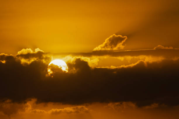 The sun rises, half visible behind a layer of clouds.