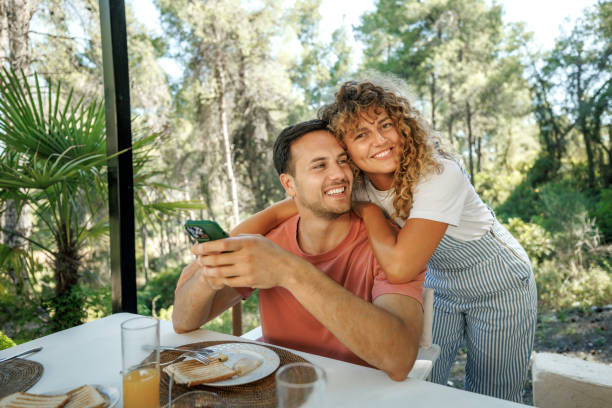 istock Cheerful young couple using smart phone while having breakfast outdoors 2198597344