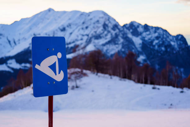 Blue sign indicating sledding, with No Ski No Snowboard written below, stands in front of snow-covered mountain range