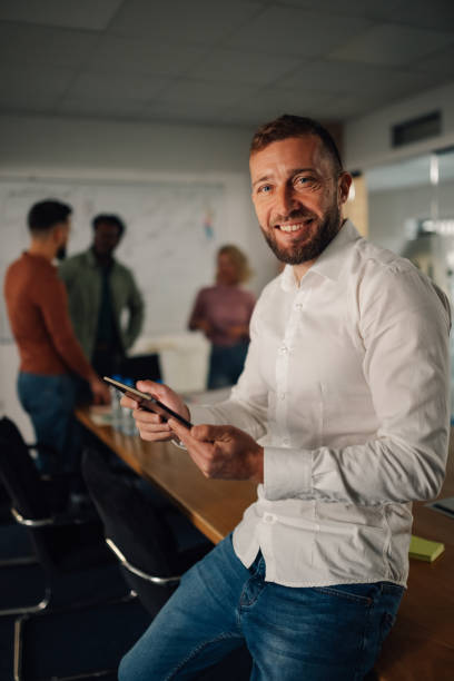 istock Smiling businessman using smartphone in modern office with colleagues 2198602306