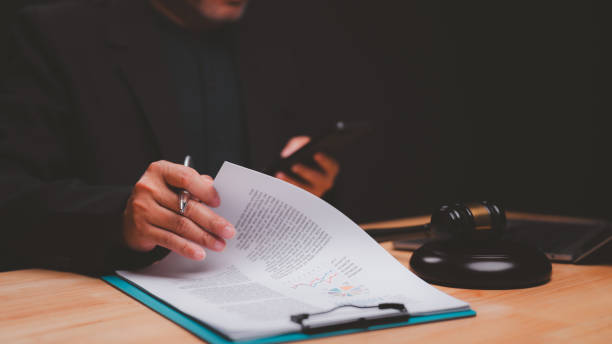 istock Legal professional examines important documents while holding smartphone, surrounded by gavel and laptop, symbolizing intersection of law and technology in modern practice 2198604818