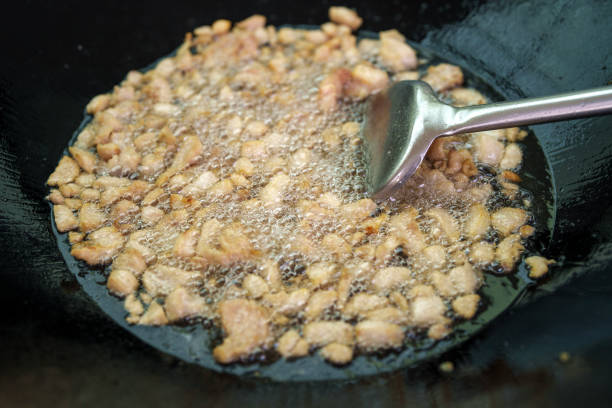 Golden-brown crispy pork lard frying in hot oil inside a black wok, with bubbles forming around the sizzling pieces. A metal spatula is used to stir the cooking process.