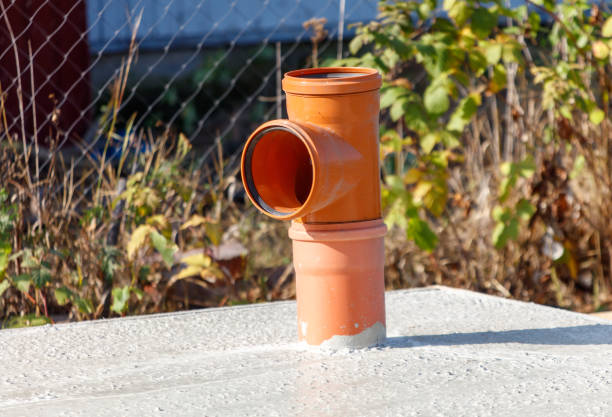 A pipe is sitting on a cement slab with a green bush in the background. The pipe is orange and has a black cap