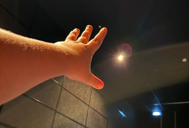 A hand is raised in the air with a light shining on it. The light is coming from a ceiling light. Scene is uplifting and positive