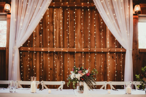 istock Indoor barn wedding reception with head table with string lights and flowers 2198637843