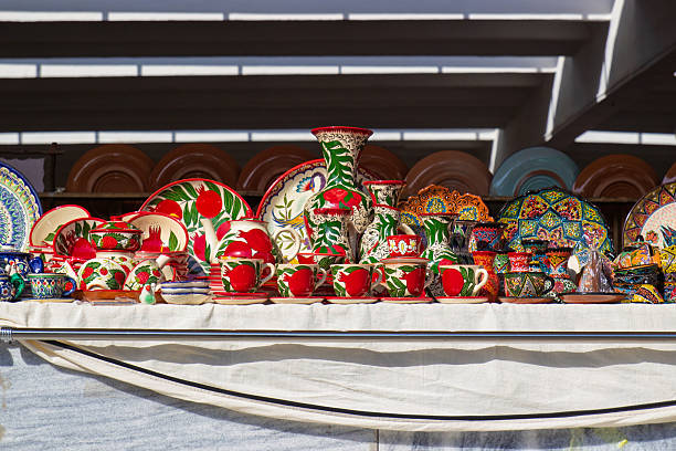 Sale of colorful sets of clay pottery with traditional national Uzbek pomegranate fruit ornament at the bazaar. Typical ceramic souvenirs selling at street vendor on local market