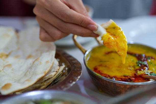A close-up of hands tearing freshly baked naan bread, served with flavorful dal tadka, rice, and masala milk tea in an Indian restaurant.