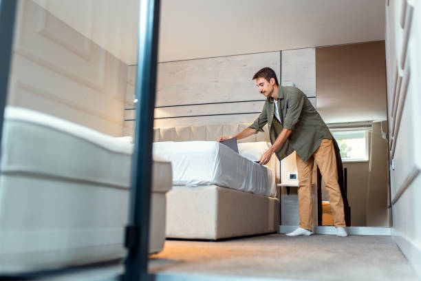 istock Man standing next to the bed in bedroom using laptop. 2198643427