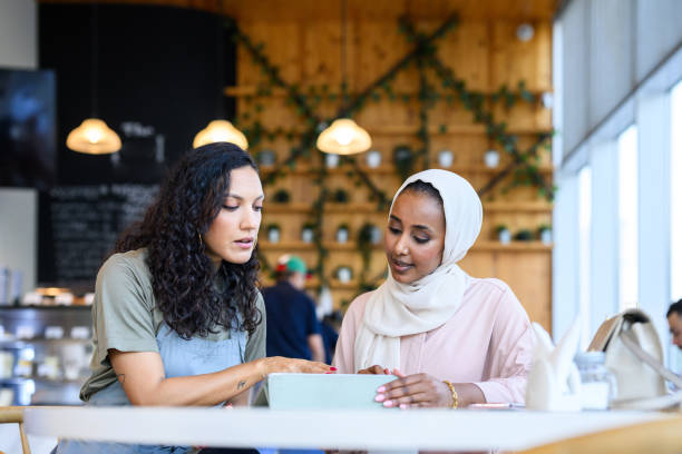 istock Cafe owner pointing at digital tablet in discussion with Middle Eastern woman 2198644025