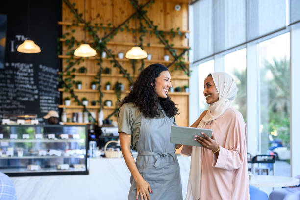 istock Cafe owner and Middle Eastern woman standing smiling at each other using digital tablet 2198644048