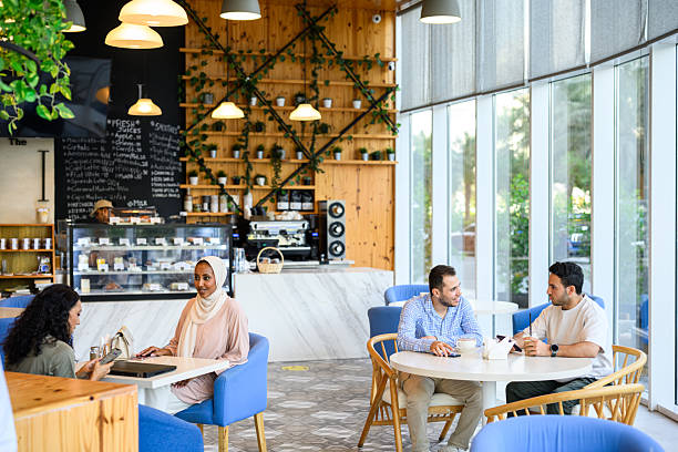 Small group of young professionals having cheerful discussions and meetings at cafe tables. Young Middle Eastern people sitting in a coffee shop in business casual.