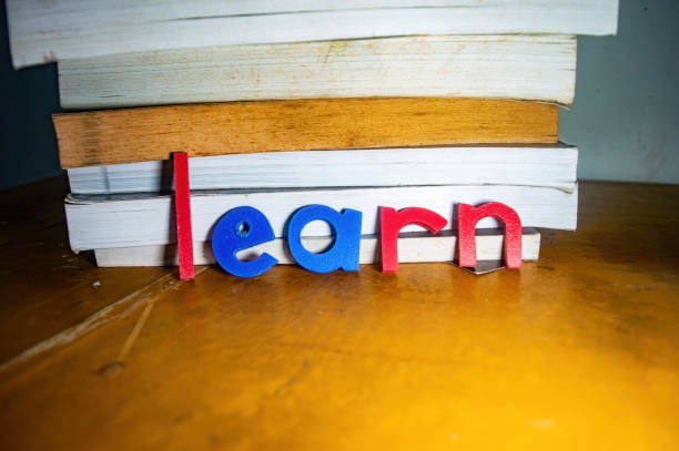 A stack of books on a wooden table with colorful letters spelling learn in front, symbolizing education and knowledge. The image emphasizes the importance of learning and academic growth