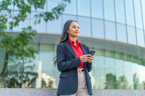 istock Young Professional Woman Using Smartphone with Modern Office Building Background 2198646024