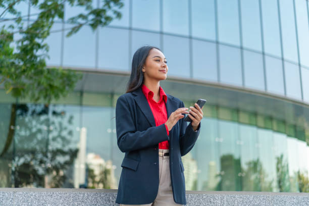 istock Young Professional Woman Using Smartphone with Modern Office Building Background 2198646041