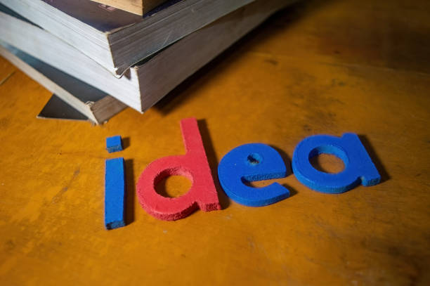 Colorful foam letters spelling idea on a wooden surface with a stack of books in the background, symbolizing creativity and knowledge