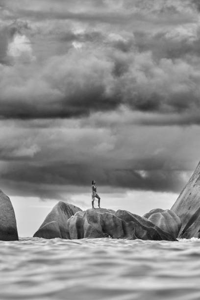 Black an white photography of sensual woman in bikini standing on a rock during summer day at Anse Source d'Argent beach. Copy space.