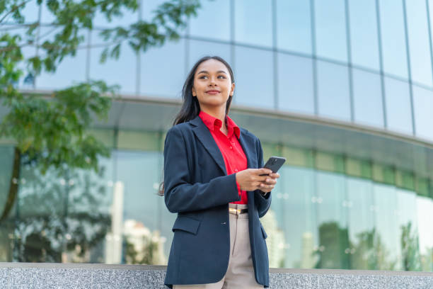 istock Young Professional Woman Using Smartphone with Modern Office Building Background 2198646369