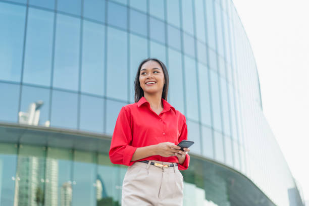istock Young Professional Woman Using Smartphone with Modern Office Building Background 2198646399