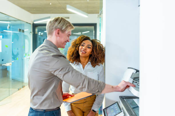 Two coworkers using a modern multifunction printer in a coworking office, collaborating on a printing task
