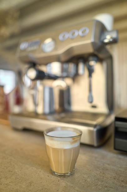 Freshly brewed cappuccino sits on cafe counter, ready to be served, with coffee machine in background