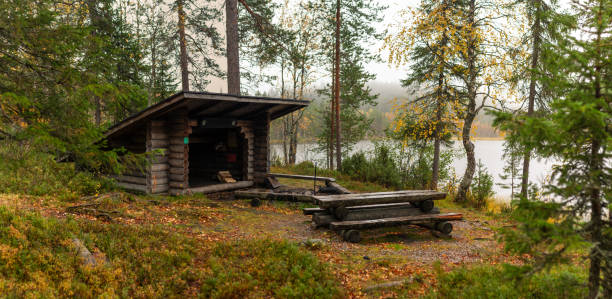 istock Rustic Camping Wilderness Shelter with Wooden Benches and Firepit Amidst Autumn Forest by Tranquil Lake 2198648510