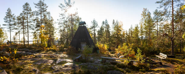 Rustic Finnish kota with fire pit and seating in a serene forest clearing bathed in golden autumn sunlight, providing a peaceful retreat for hikers and nature lovers. Captured in Finland, Europe.