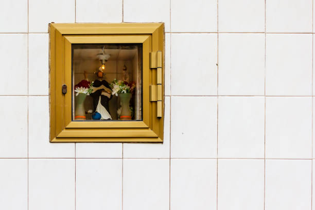 A serene religious shrine built into a golden box, featuring a statue and flowers against a decorative tiled wall.