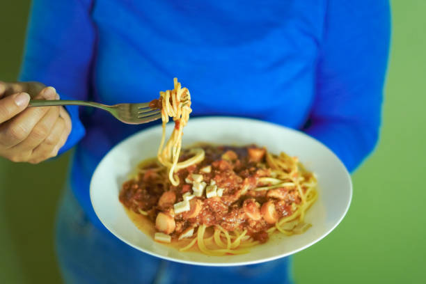 Woman hand holding a plate of spaghetti on a green wall.